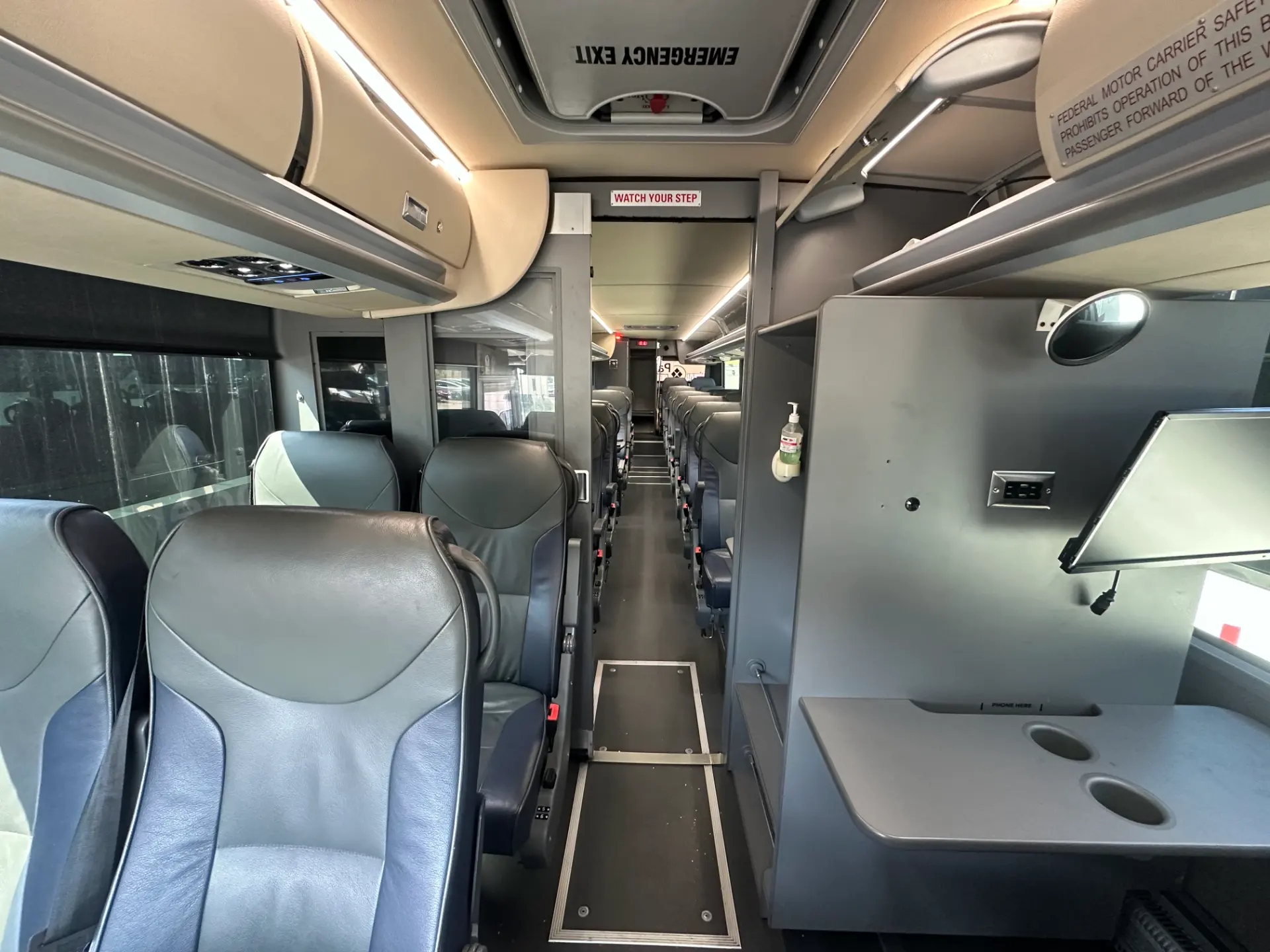 Interior view of the Four Season Travel Mini Coach showing passenger seating, the center aisle, overhead storage, and the table area with cupholders