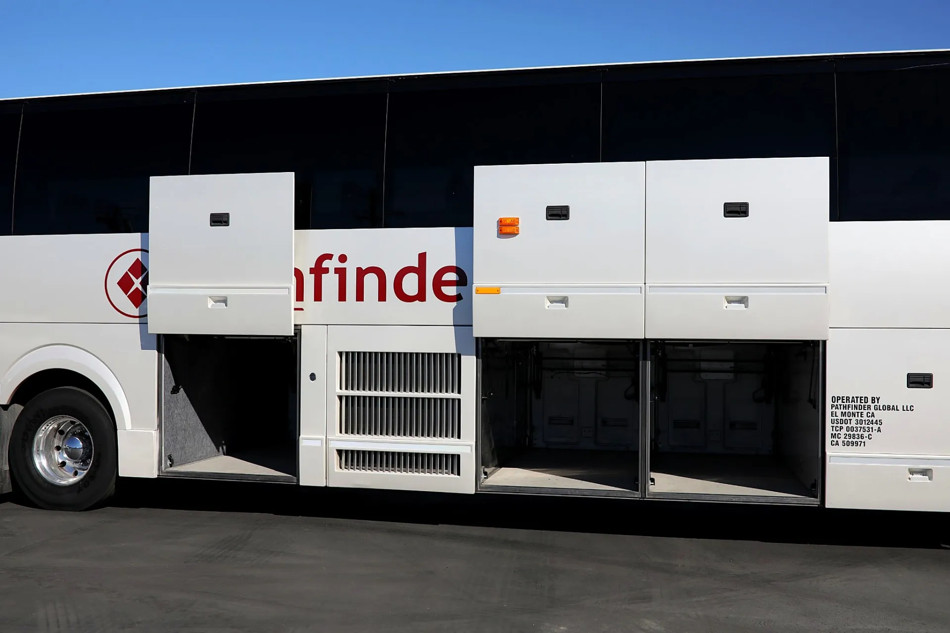 Under-floor luggage compartments open along the side of a Four Season Travel motorcoach during trip preparation